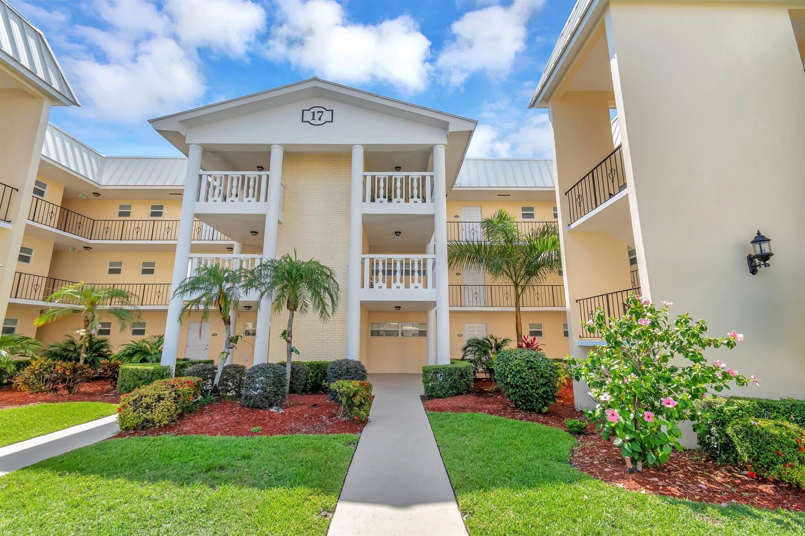 A three-story apartment building exterior with white columns, balconies, and landscaped grounds — 17 Colonial Club Drive # 204, Boynton Beach FL 33435, BOYNTON BEACH, FL