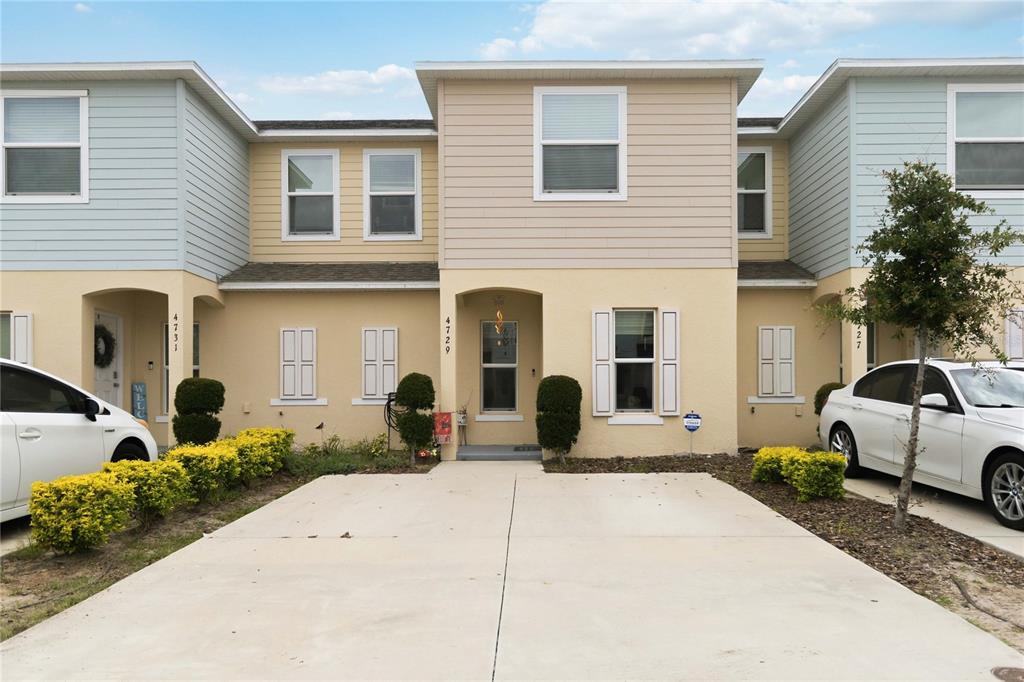 A row of three attached townhomes features beige stucco, light blue siding, and concrete driveways — 4729 CORAL CASTLE DRIVE, KISSIMMEE, FL