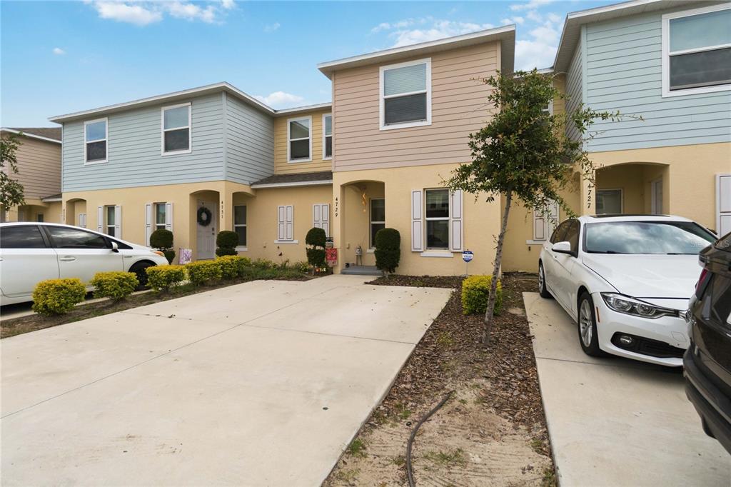 A row of two-story townhouses with beige stucco, light blue siding, and concrete driveways — 4729 CORAL CASTLE DRIVE, KISSIMMEE, FL