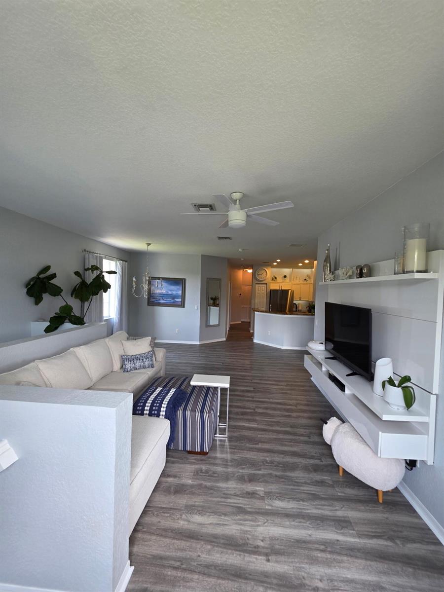 A living room features light gray walls, wood-look flooring, a white sectional, and floating shelves — 1560 SE Hampshire Way # 204, Stuart FL 34994, STUART, FL
