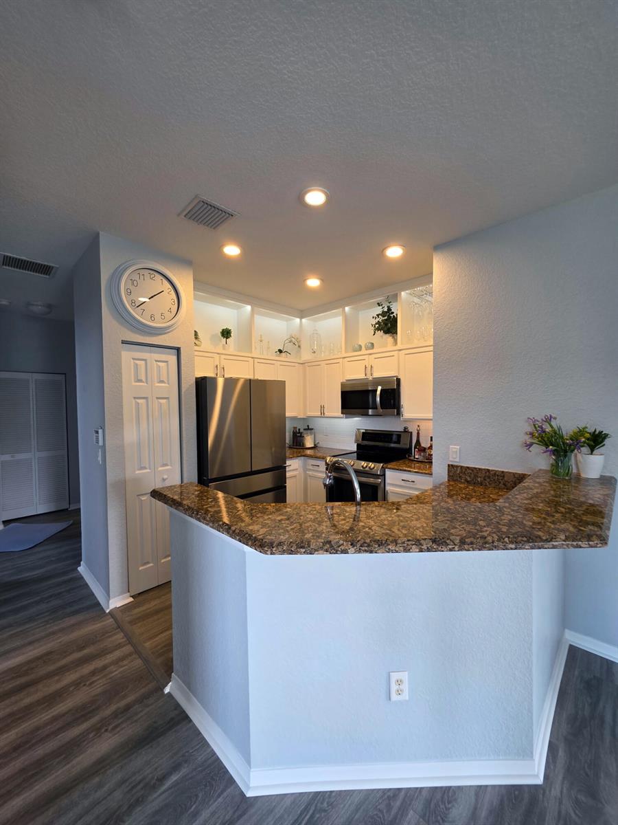 A kitchen features white cabinets, stainless steel appliances, and a brown granite breakfast bar — 1560 SE Hampshire Way # 204, Stuart FL 34994, STUART, FL