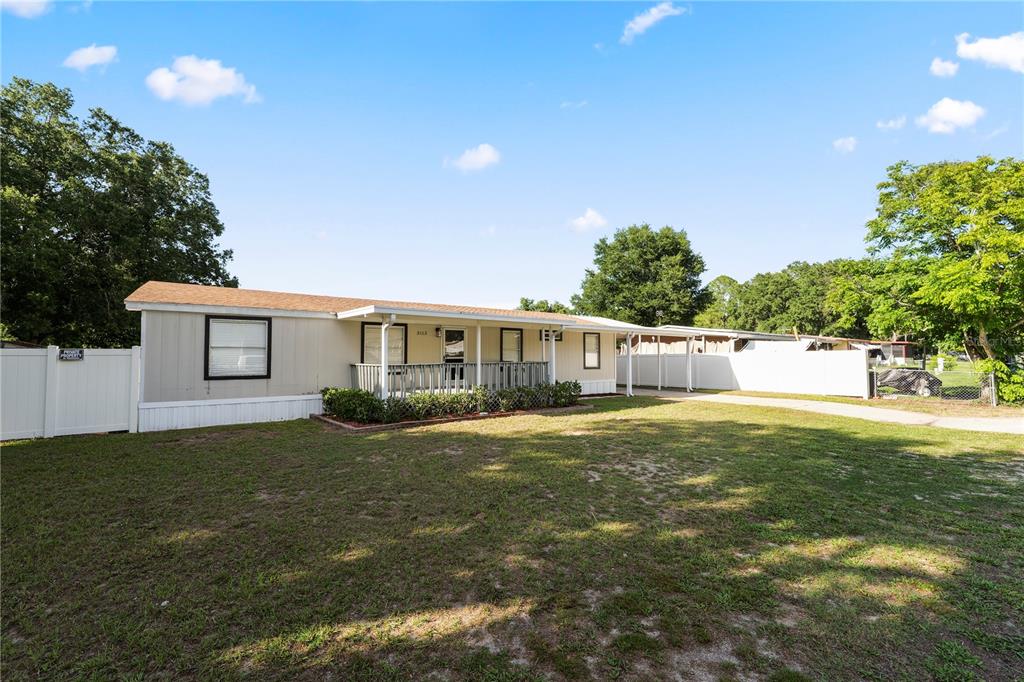 A single-story manufactured home features a front porch, tan siding, and a white fence — 3113 ROLLINGLEN LANE, LAKELAND, FL