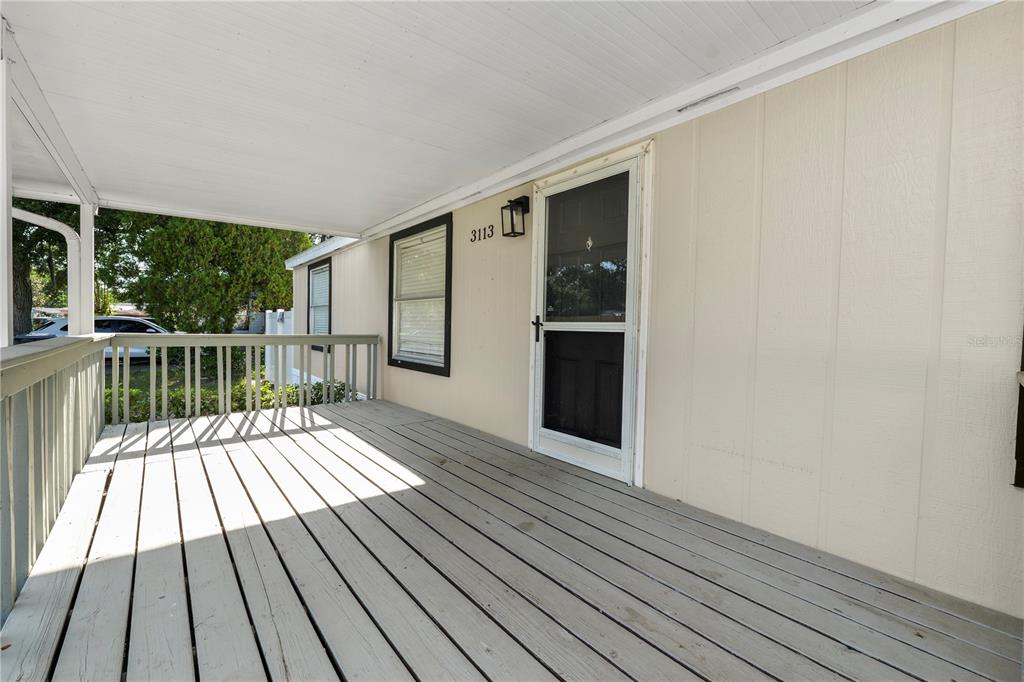 A covered wooden porch features a white door with a screen and light-colored siding — 3113 ROLLINGLEN LANE, LAKELAND, FL