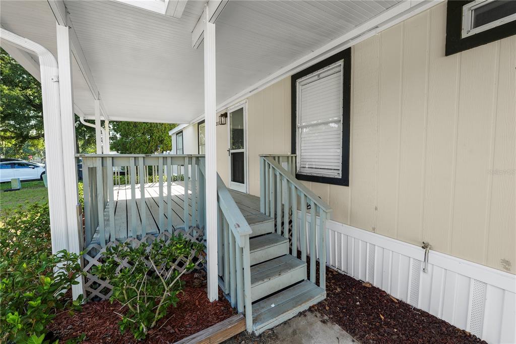 A covered wooden porch with stairs leads to the entrance of a beige mobile home — 3113 ROLLINGLEN LANE, LAKELAND, FL