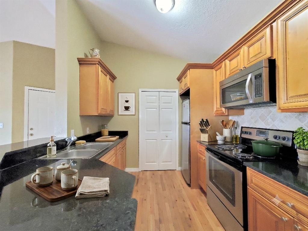 A kitchen features light wood cabinets, black countertops, stainless steel appliances, and hardwood flooring — 5959 WESTGATE DRIVE UNIT 1535, ORLANDO, FL