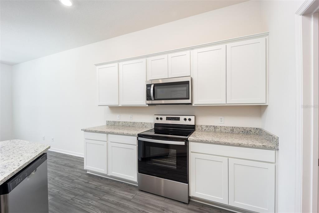 A kitchen features white cabinets, granite countertops, and stainless steel appliances over wood-look flooring — 697 POPPY LANE, DUNDEE, FL