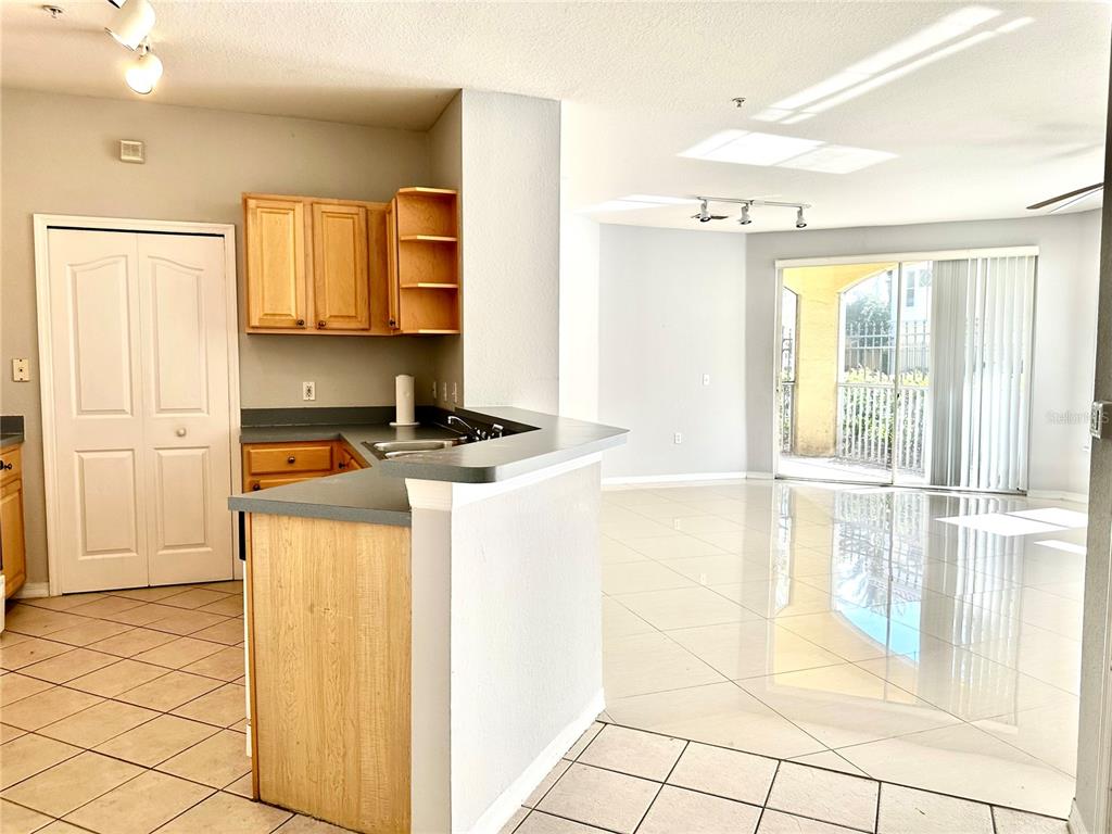 A kitchen with light wood cabinets and gray countertops opens into a bright living area — 1150 LAKE SHADOW CIRCLE UNIT 3102, MAITLAND, FL