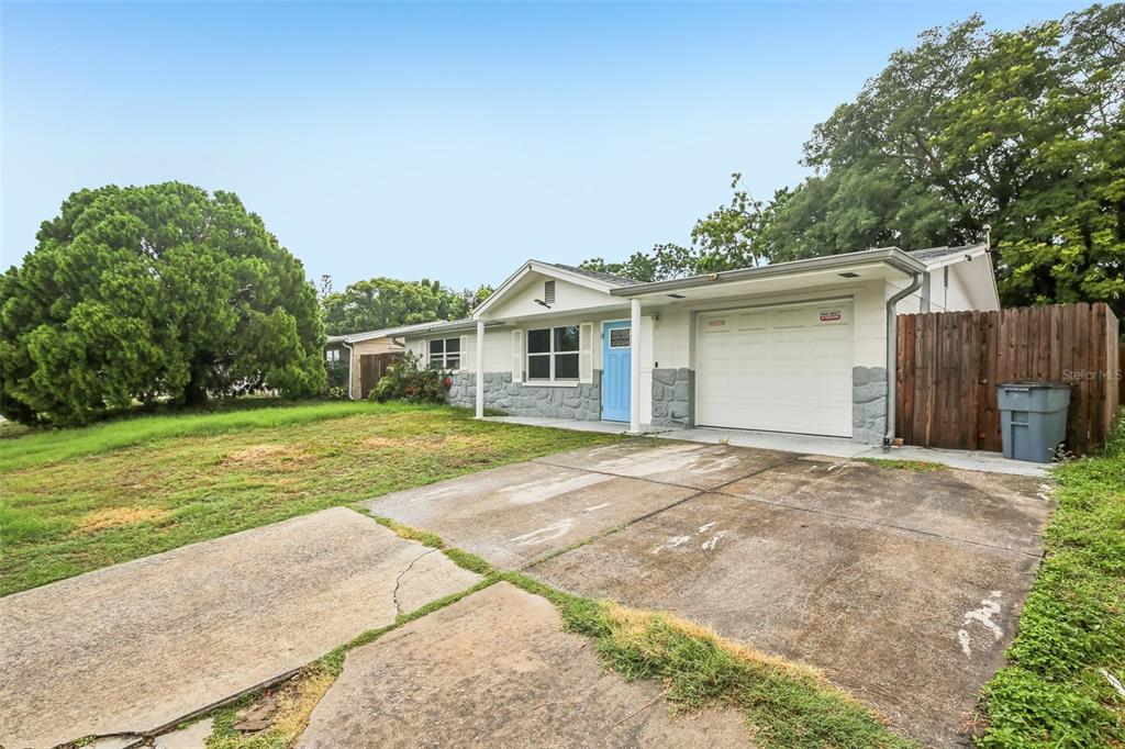 A single-story house with a light-colored exterior, stone accents, a blue front door, and driveway — 10911 GAWAIN ROAD, PORT RICHEY, FL