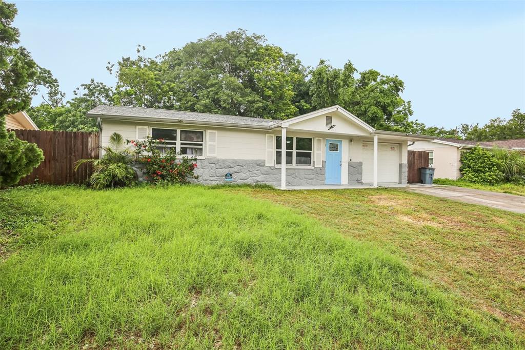 A single-story house with light siding, a stone base, and a bright blue front door — 10911 GAWAIN ROAD, PORT RICHEY, FL
