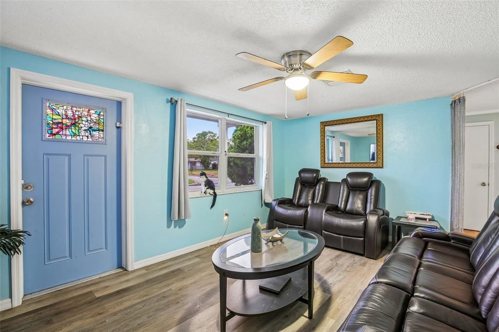 A living room features light blue walls, wood-look flooring, leather furniture, and a ceiling fan — 10911 GAWAIN ROAD, PORT RICHEY, FL