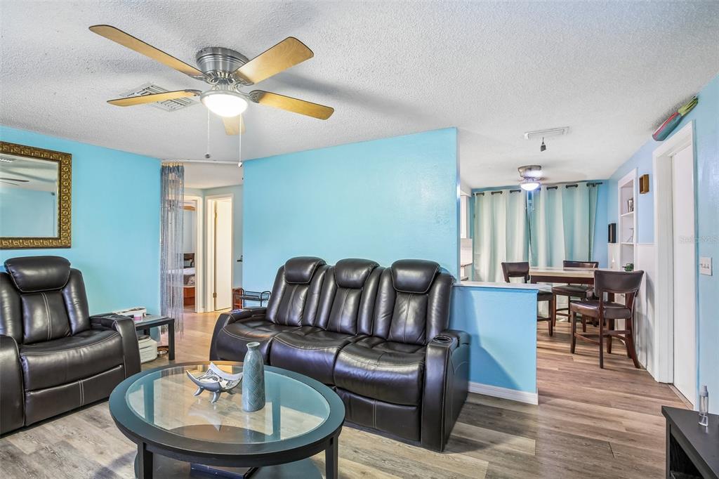 A living room with light blue walls, dark leather furniture, and wood-look flooring — 10911 GAWAIN ROAD, PORT RICHEY, FL