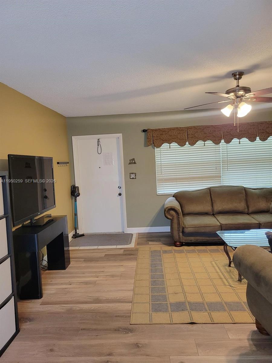 A living room features wood-look flooring, a sofa, a television, and a ceiling fan — 2031 Dewey St # 302, Hollywood FL 33020, HOLLYWOOD, FL