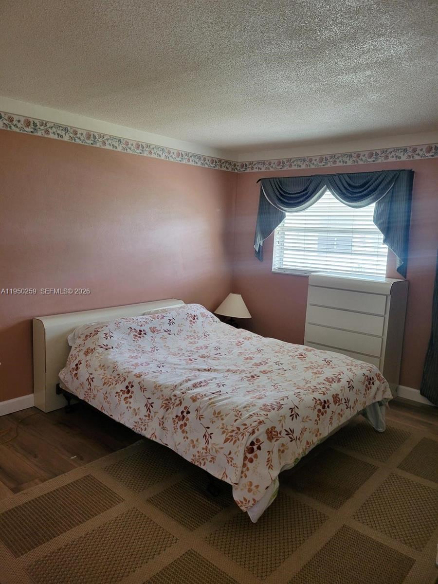 A bedroom features a bed with a floral comforter, a white dresser, and pink walls — 2031 Dewey St # 302, Hollywood FL 33020, HOLLYWOOD, FL