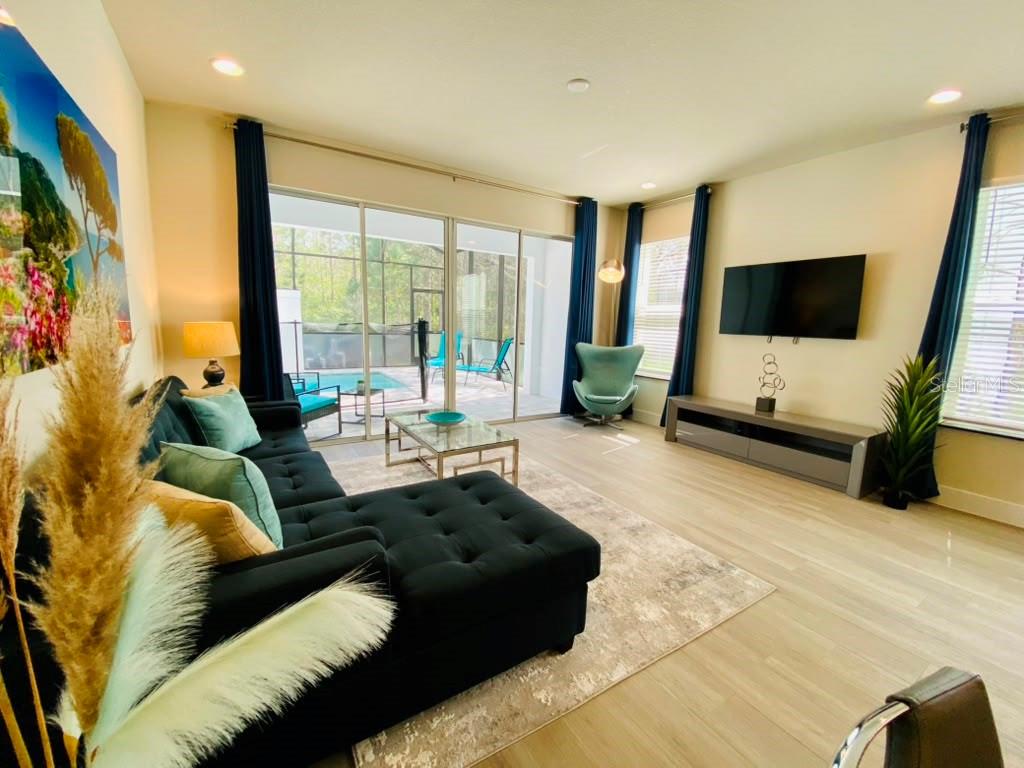 A living room with a black sectional sofa, glass coffee table, and sliding doors to a pool — 17214 BLESSING DRIVE, CLERMONT, FL