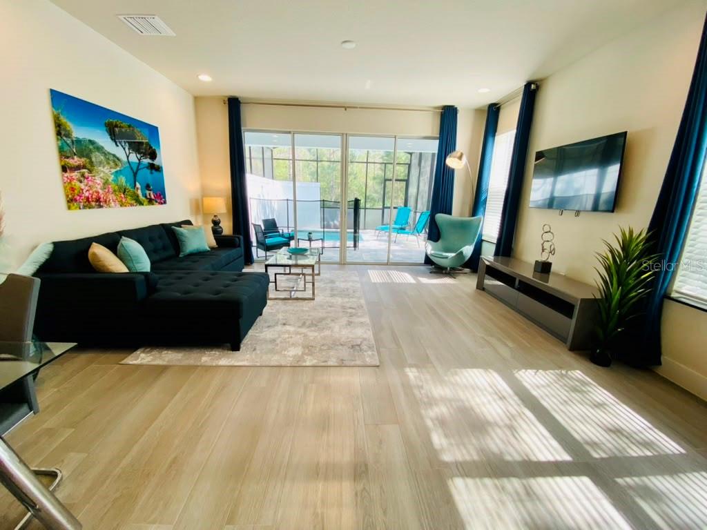 A living room with a black sectional, light wood floors, and a view of a pool — 17214 BLESSING DRIVE, CLERMONT, FL