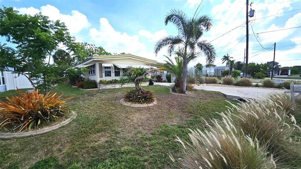 A light-colored mobile home sits on a grassy lot with palm trees and landscaping — 1240 SEAGULL DRIVE, ENGLEWOOD, FL
