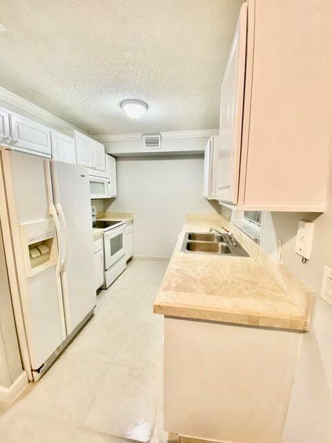 A kitchen features white cabinets, a stainless steel refrigerator, and a beige countertop — 3303 Kirk Road # 1, Lake Worth FL 33461, LAKE WORTH, FL