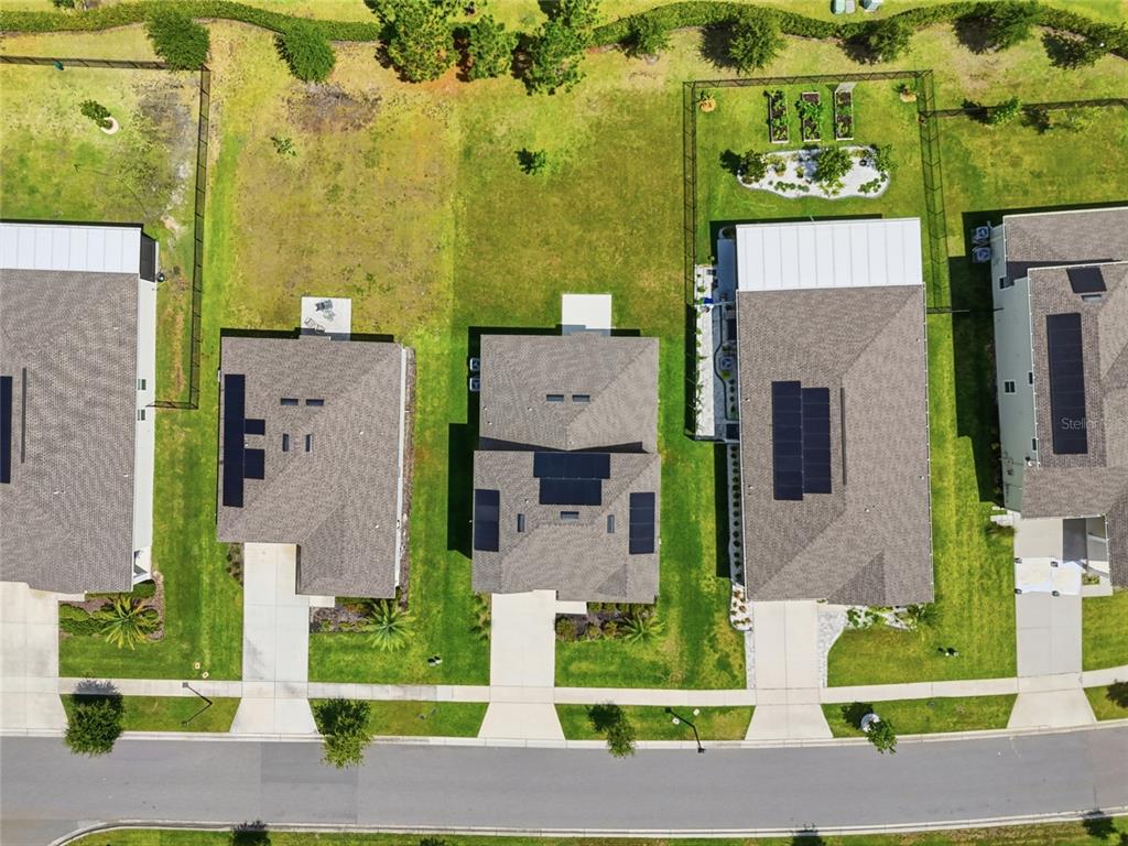 An aerial view shows three suburban houses with solar panels on their roofs and driveways — 5215 TANZANITE DRIVE, MOUNT DORA, FL