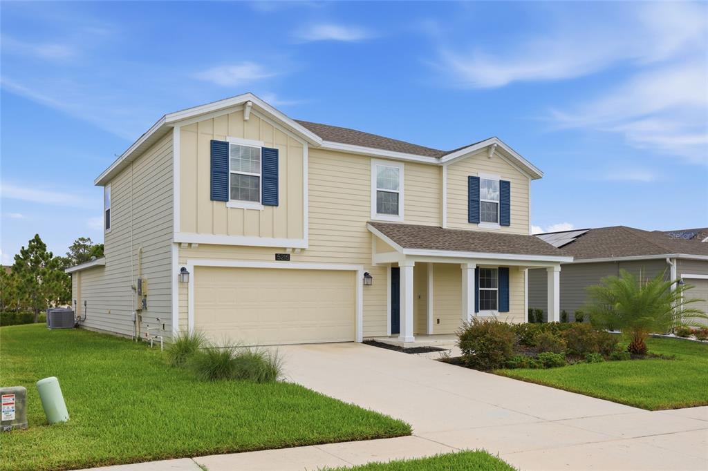 A two-story, light yellow suburban house with a two-car garage and blue shutters — 5215 TANZANITE DRIVE, MOUNT DORA, FL