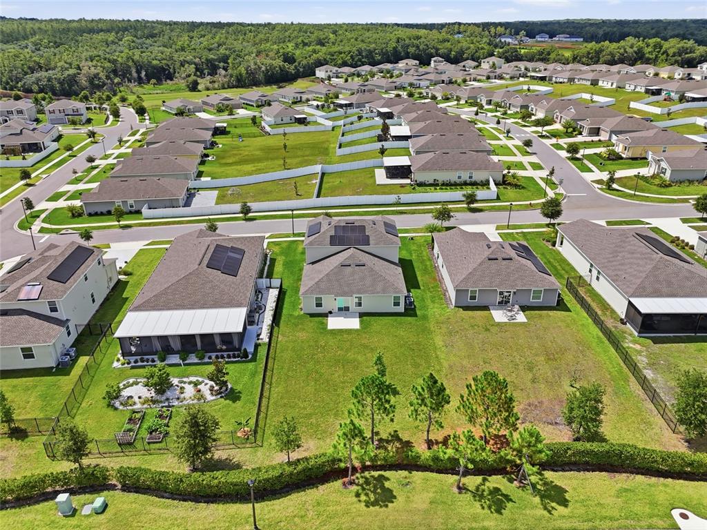 An aerial view shows several suburban houses with fenced backyards and solar panels on roofs — 5215 TANZANITE DRIVE, MOUNT DORA, FL