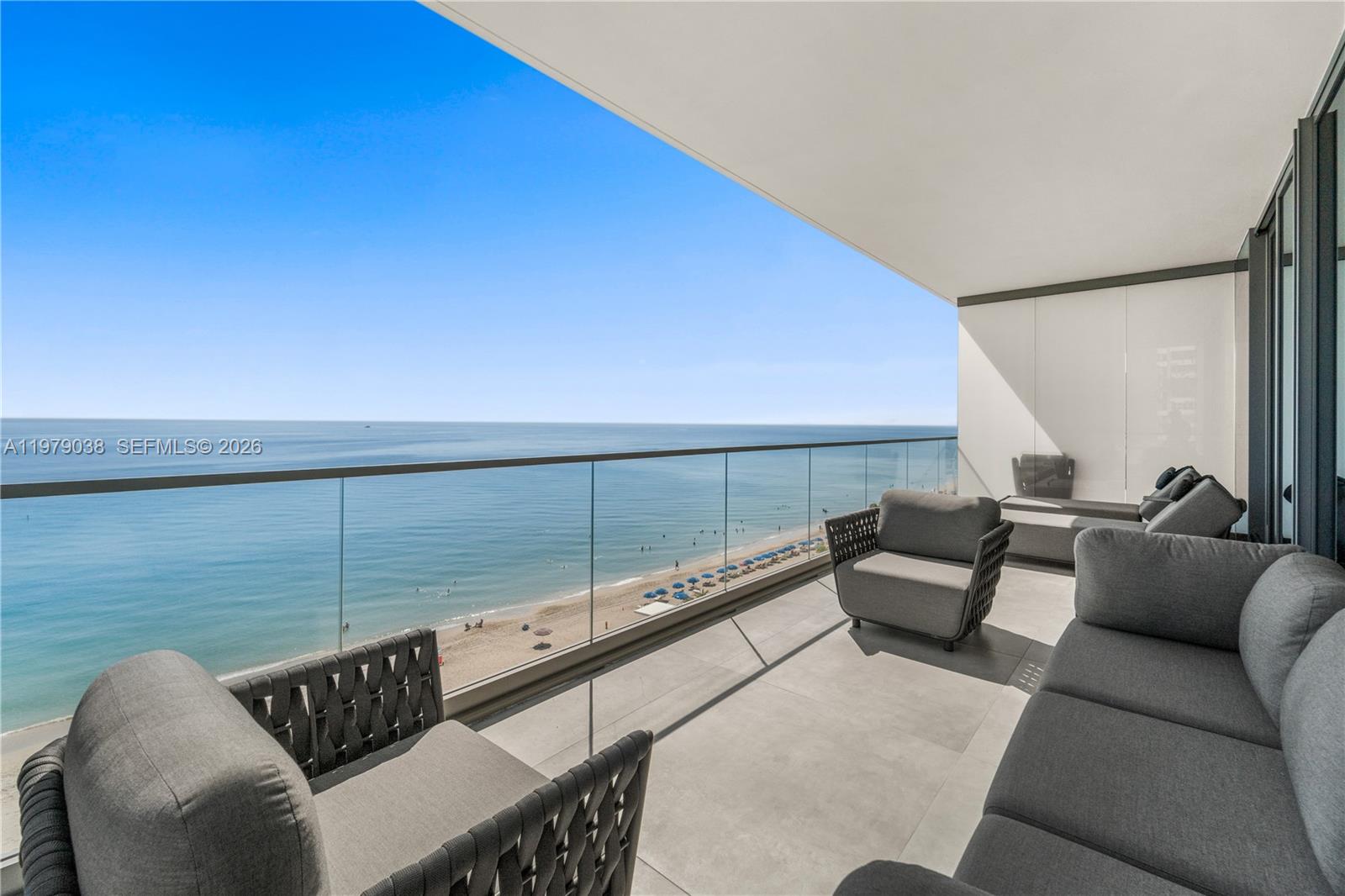 A balcony with modern gray furniture overlooks a sandy beach and the ocean — 2000 S Ocean Dr # 8A, Hallandale Beach FL 33009, HALLANDALE BEACH, FL