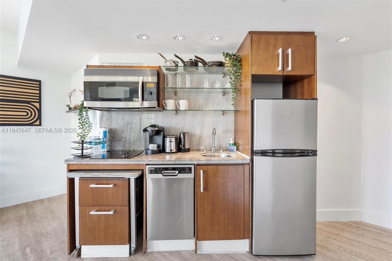 A compact kitchen features stainless steel appliances, wood cabinetry, and open glass shelving — 1060 Ocean Dr # D303, Miami Beach FL 33139, MIAMI BEACH, FL