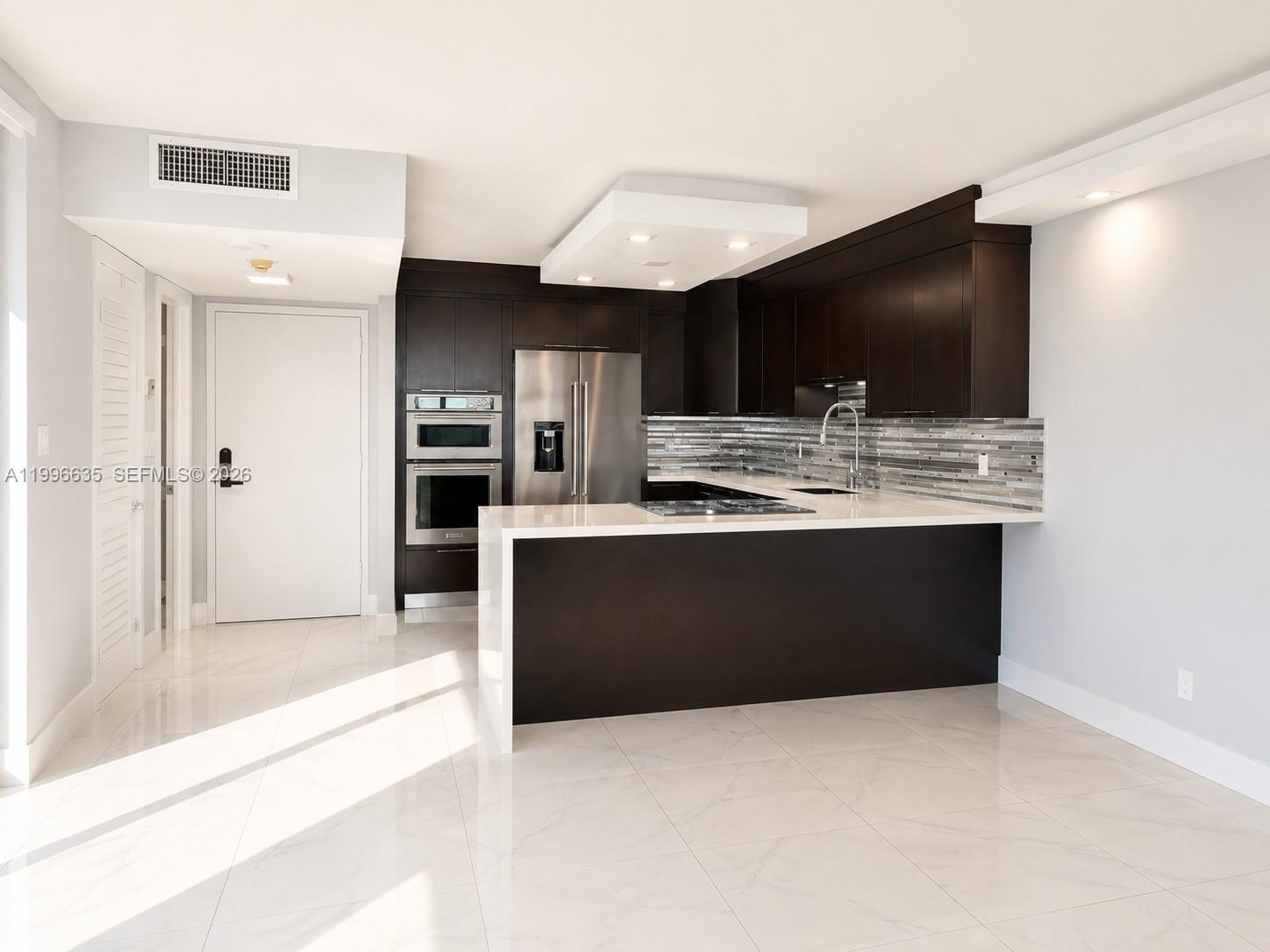 A modern kitchen features dark wood cabinetry, stainless steel appliances, and a white waterfall island — 1420 Brickell Bay Dr # 702E, Miami FL 33131, MIAMI, FL