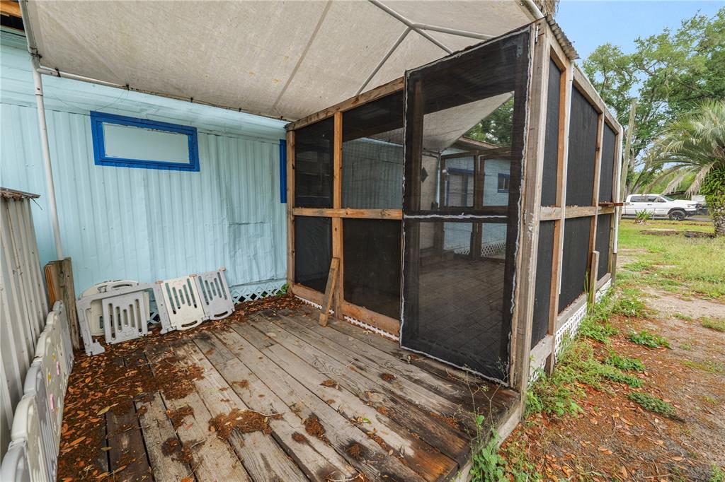 A wooden deck with a screened-in enclosure sits beside a light blue mobile home — 829 NASHVILLE ROAD, LAKELAND, FL