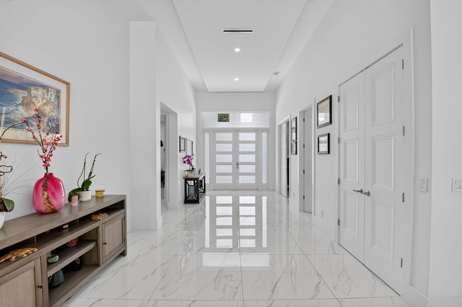 A bright, white hallway features marble-look tile flooring, a tray ceiling, and double front doors — 711 NE 6th Street, Boca Raton FL 33432, BOCA RATON, FL