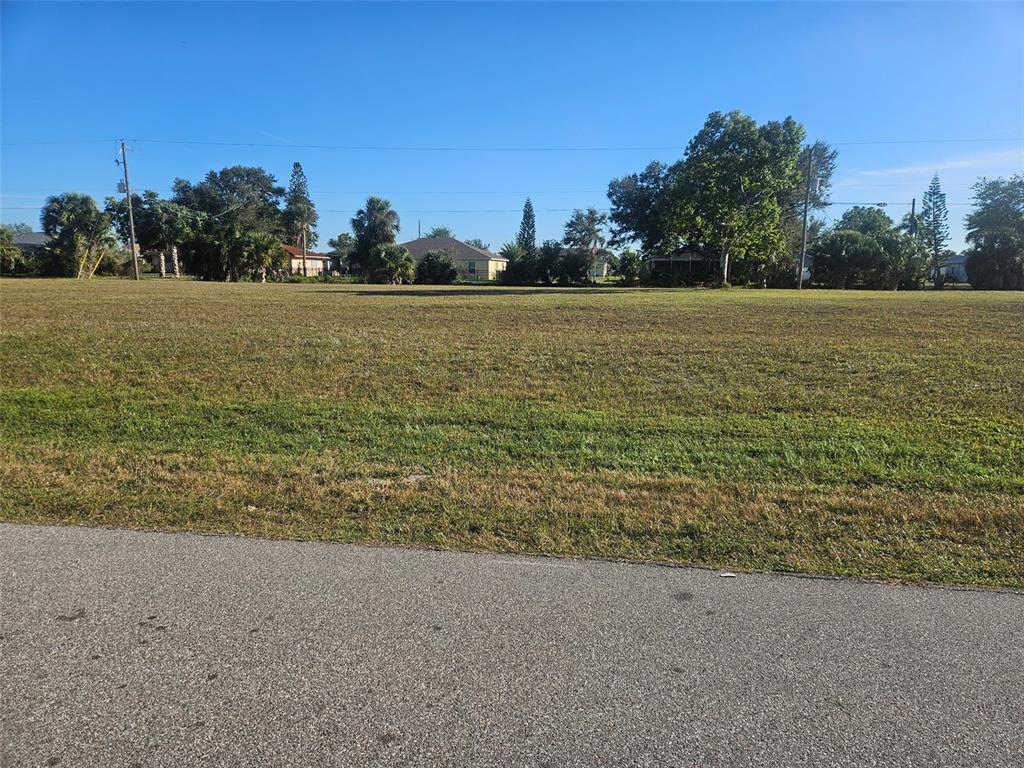 A large, flat, grassy vacant lot sits adjacent to an asphalt road under a clear sky — 25237 CADIZ DRIVE, PUNTA GORDA, FL