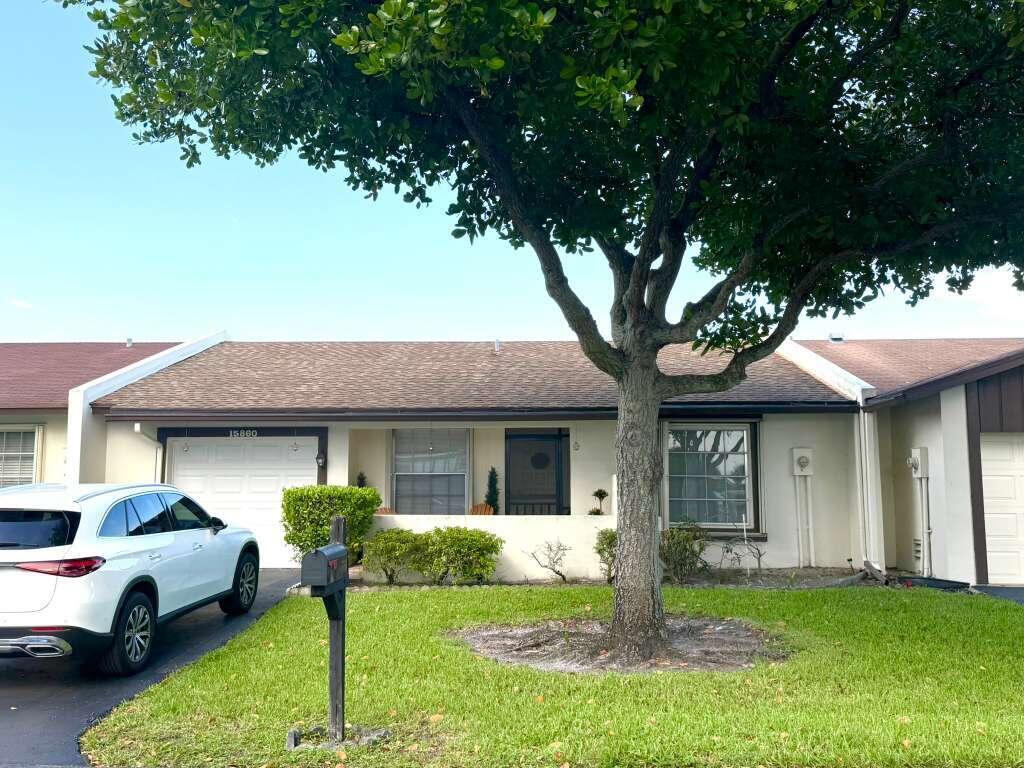 A single-story townhouse with a white exterior, a front-facing garage, and a large shade tree — 15860 Laurel Oak Circle, Delray Beach FL 33484, DELRAY BEACH, FL