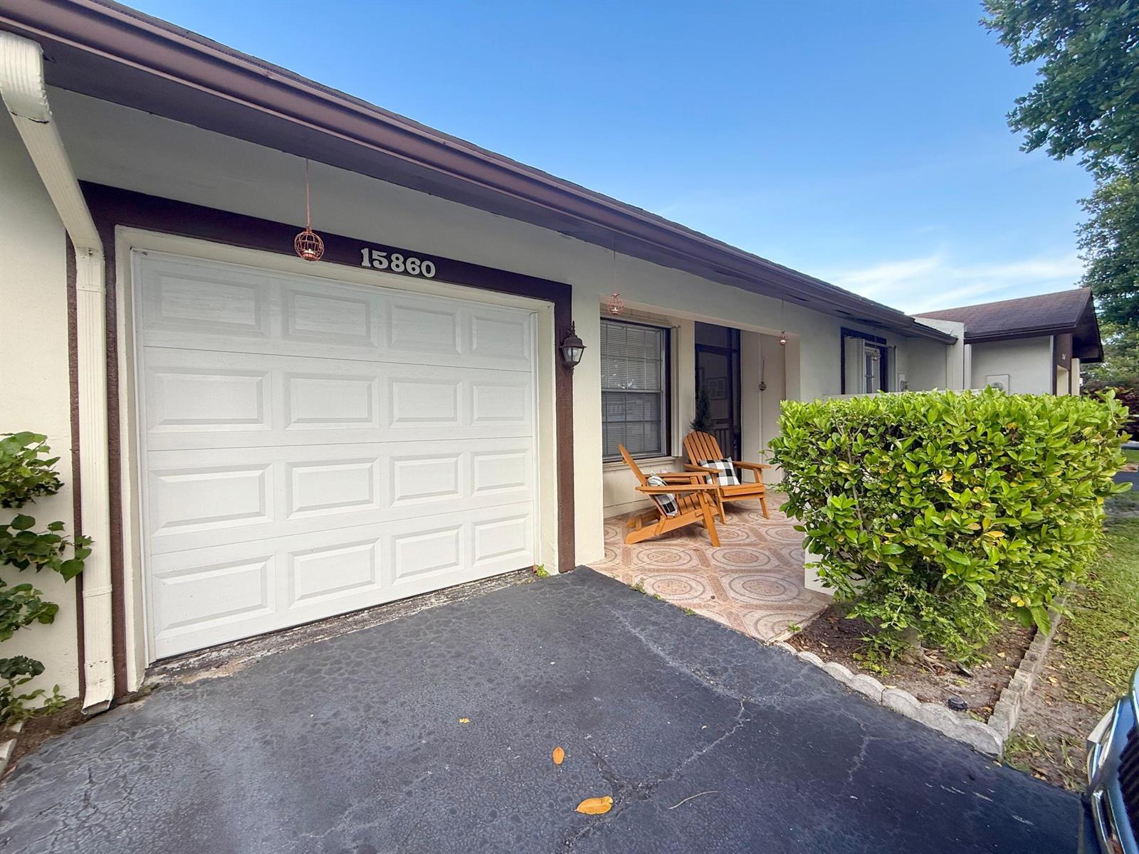 The exterior of a single-story home features a white garage, a paved patio, and landscaping — 15860 Laurel Oak Circle, Delray Beach FL 33484, DELRAY BEACH, FL