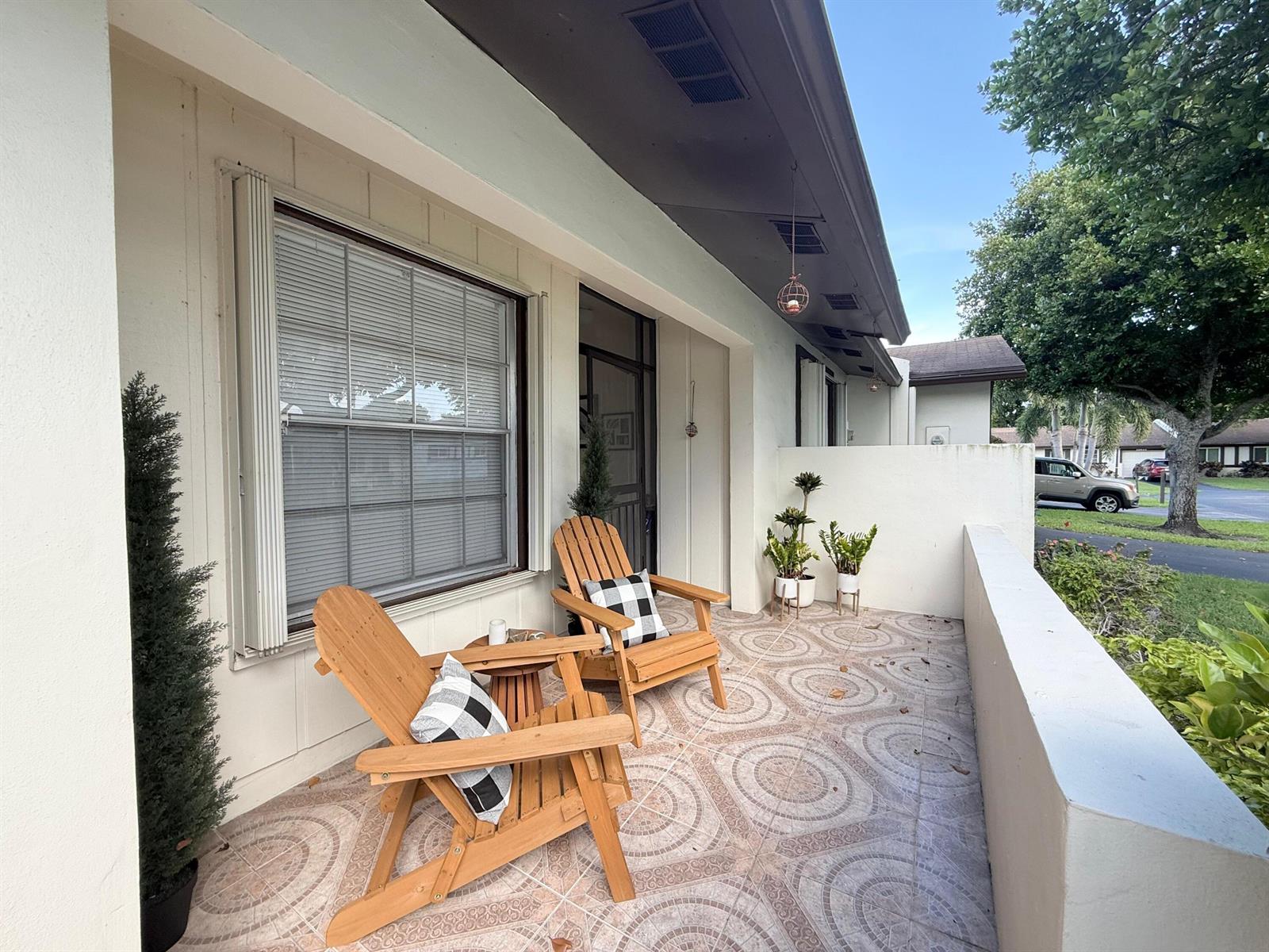 A covered patio features two wooden Adirondack chairs, patterned tile flooring, and potted plants — 15860 Laurel Oak Circle, Delray Beach FL 33484, DELRAY BEACH, FL