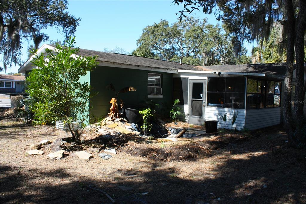 A green house exterior features a screened-in porch and a landscaped rock garden area — 2071 CANAL ROAD, DELTONA, FL