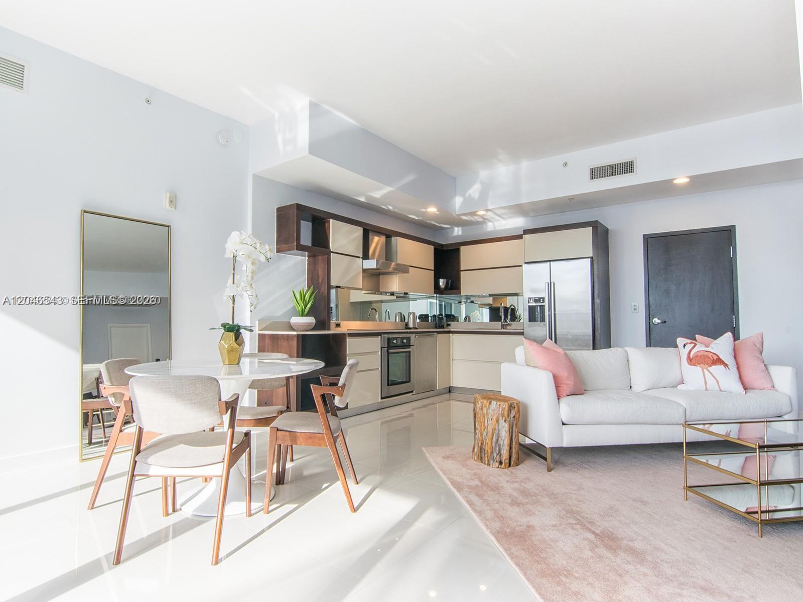 An open-concept living area features a modern kitchen, dining set, and white sofa — 2100 Park Ave # 406, Miami Beach FL 33139, MIAMI BEACH, FL