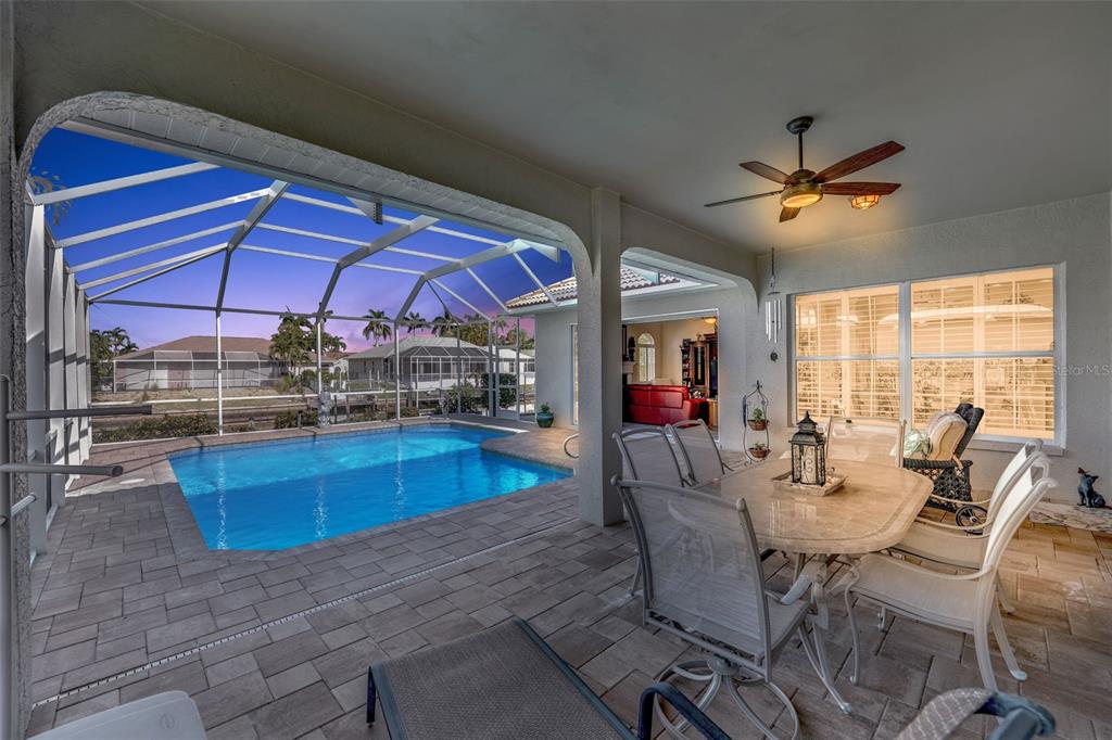 A covered patio features a dining set, ceiling fan, and a screened-in swimming pool — 5212 SW 8TH COURT, CAPE CORAL, FL