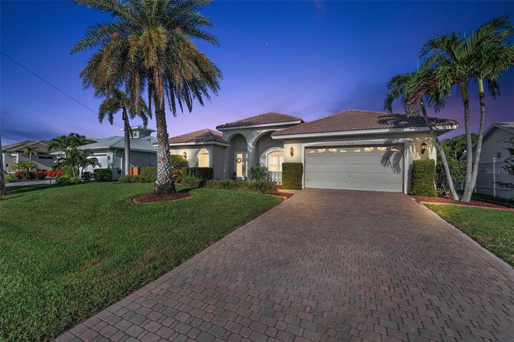 A single-story house with a paved driveway, palm trees, and a two-car garage at dusk — 5212 SW 8TH COURT, CAPE CORAL, FL