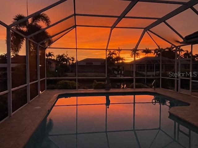 A swimming pool enclosed by a screened lanai overlooks a sunset view of neighboring houses — 5212 SW 8TH COURT, CAPE CORAL, FL
