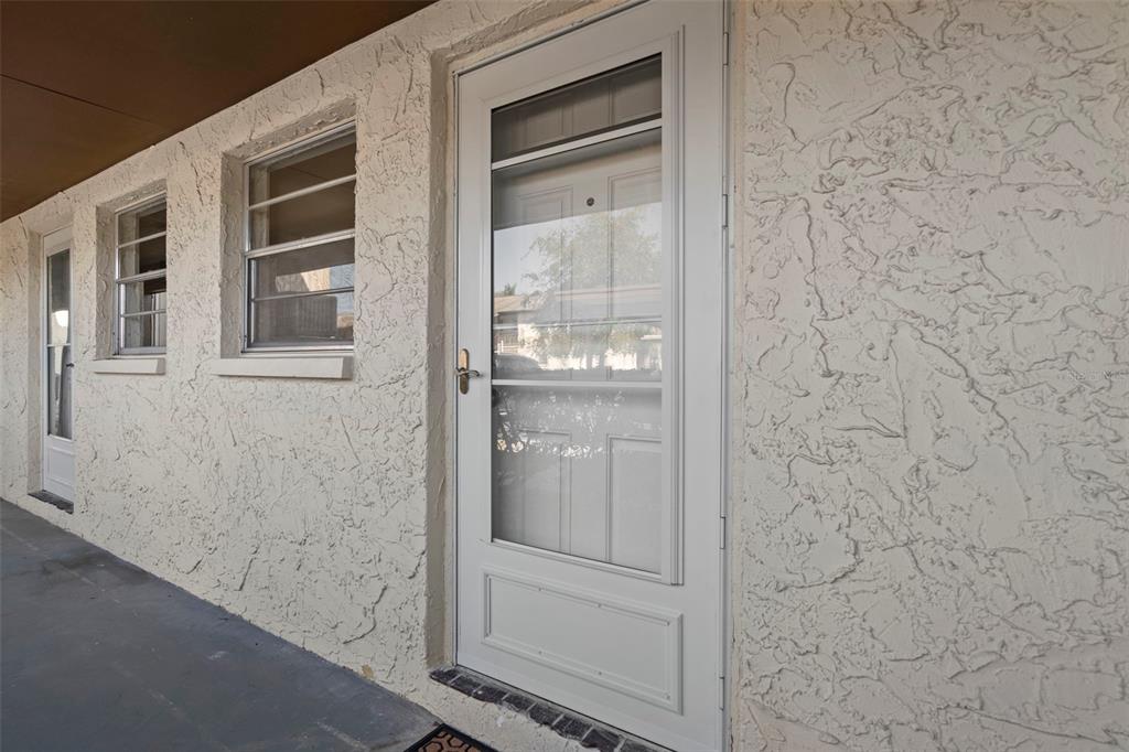 A white storm door and two windows are set into a textured stucco exterior wall — 5154 TURQUOISE LANE UNIT 106, NEW PORT RICHEY, FL