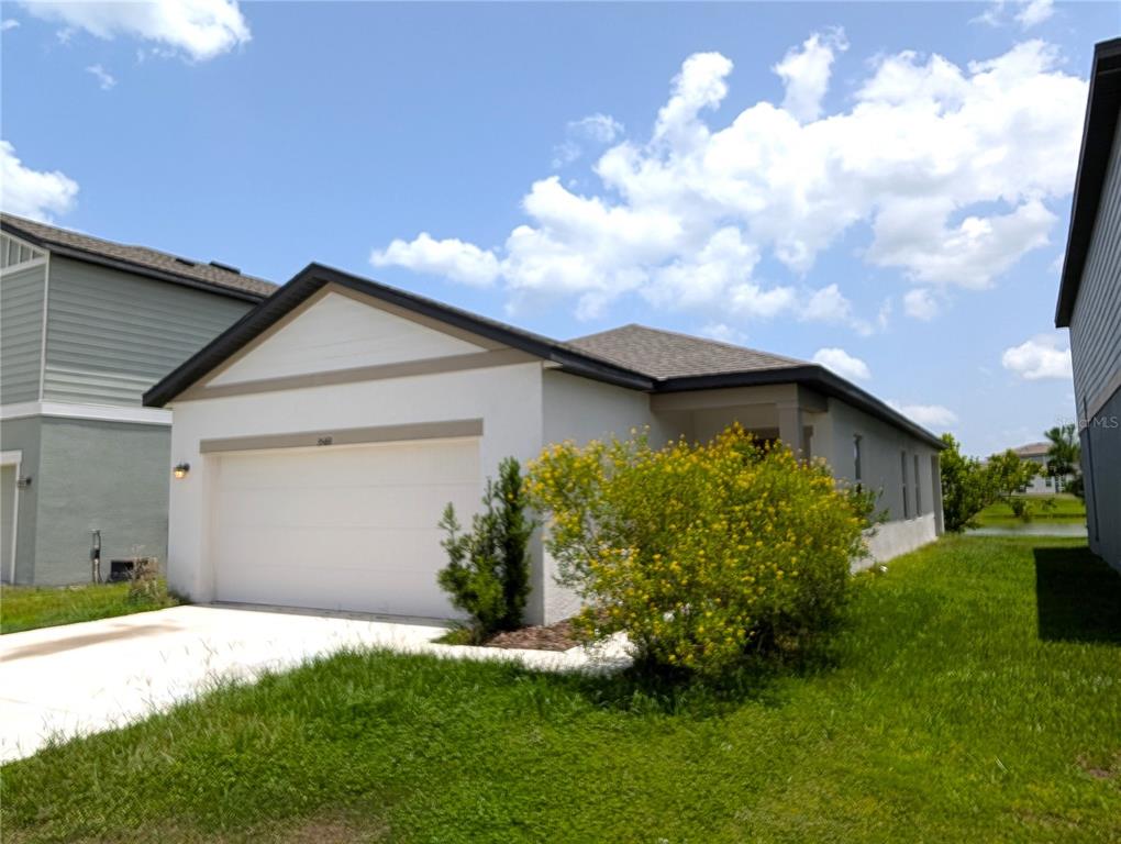 A single-story house with a white stucco facade, a two-car garage, and a yellow-flowering bush — 35491 SHADE FERN LANE, ZEPHYRHILLS, FL