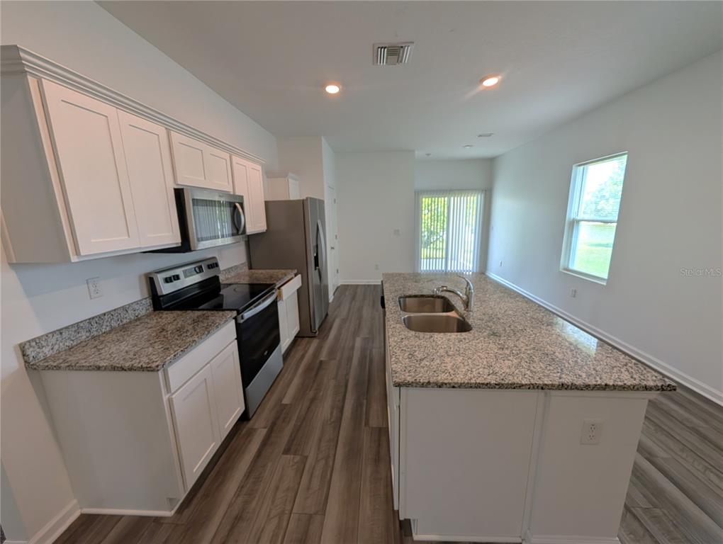 A kitchen features white cabinets, granite countertops, stainless steel appliances, and wood-look flooring — 35491 SHADE FERN LANE, ZEPHYRHILLS, FL