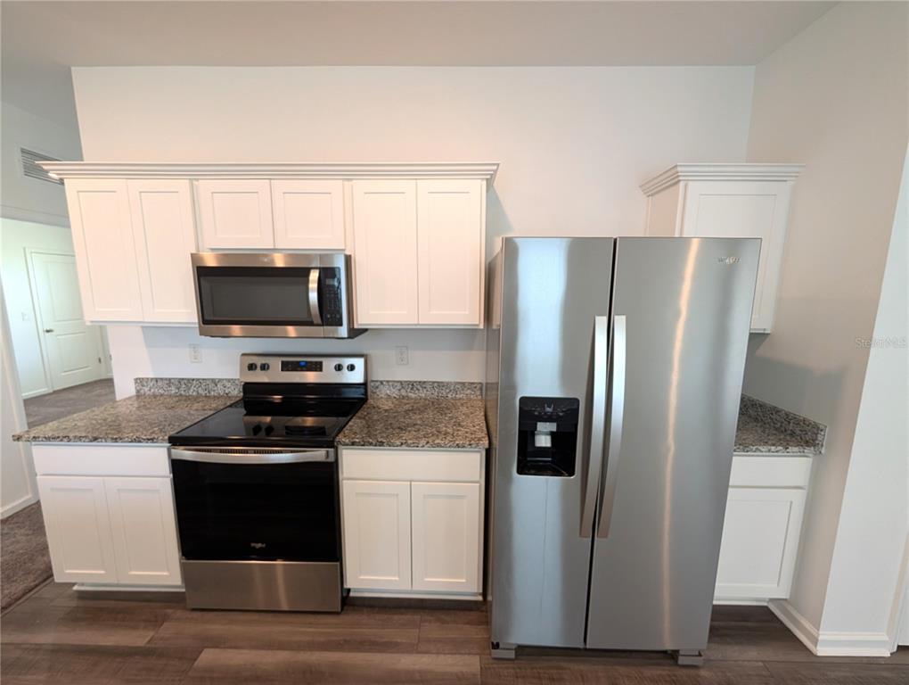 A kitchen features white cabinets, stainless steel appliances, and granite countertops — 35491 SHADE FERN LANE, ZEPHYRHILLS, FL