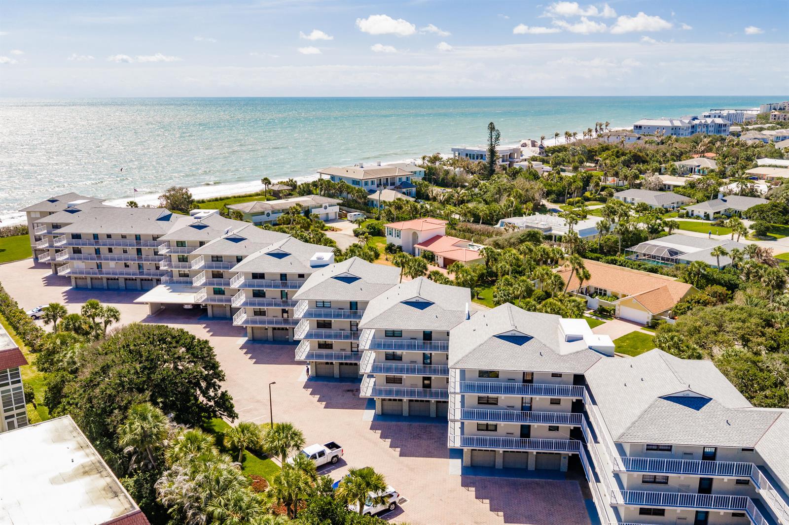 An aerial view shows a multi-story apartment complex near the ocean with paved parking — INDIAN RIVER SHORES, FL