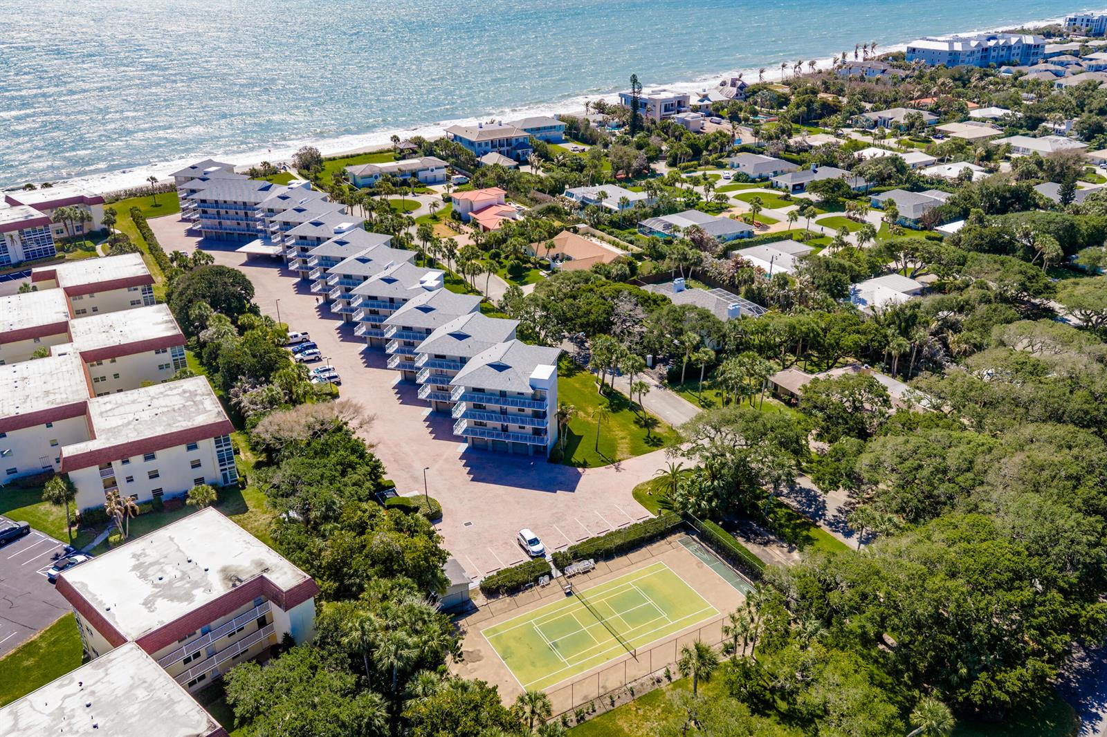 An aerial view shows a coastal condominium complex with a tennis court and parking lot — INDIAN RIVER SHORES, FL