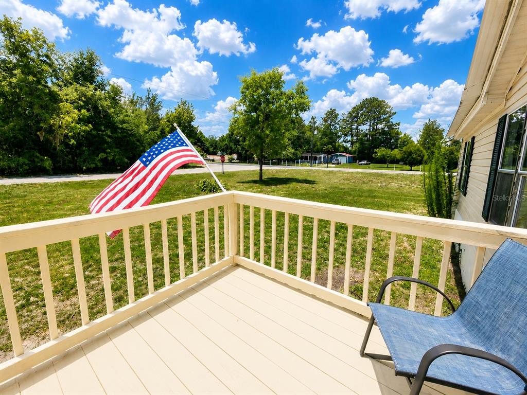 A wooden deck with a railing overlooks a grassy yard with an American flag — 13817 NE 54TH PLACE, WILLISTON, FL