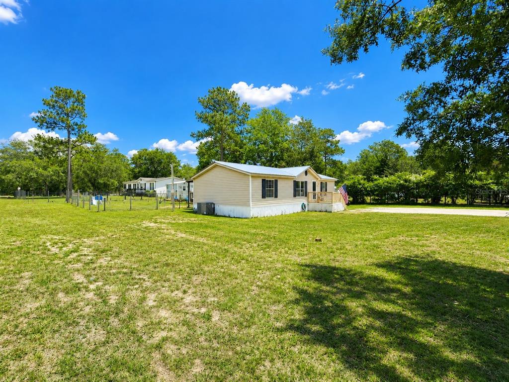 A light-colored mobile home sits on a large grassy lot under a blue sky — 13817 NE 54TH PLACE, WILLISTON, FL