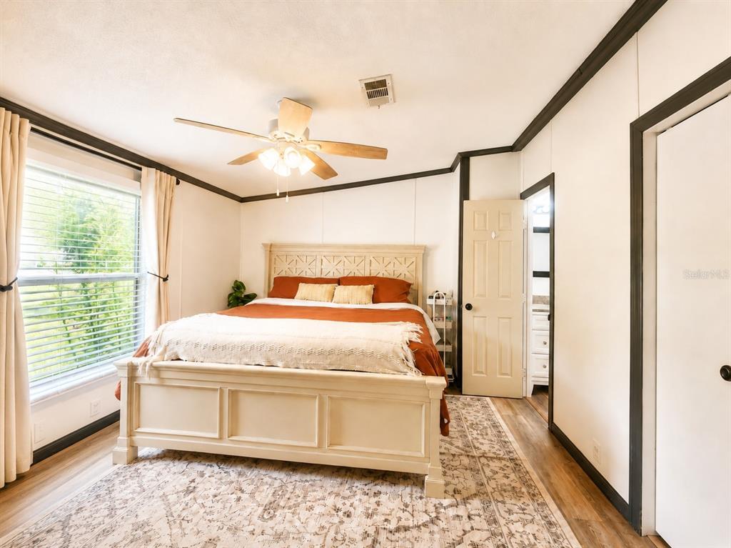 A bedroom features a light-colored bed frame, rust-colored bedding, a ceiling fan, and wood flooring — 13817 NE 54TH PLACE, WILLISTON, FL