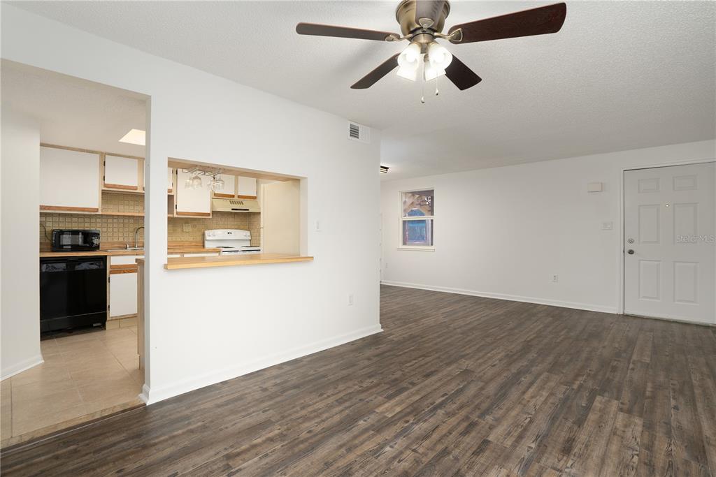 A living room with wood-look flooring and a ceiling fan opens to a kitchen area — 22291 WESTCHESTER BOULEVARD UNIT 301, PORT CHARLOTTE, FL