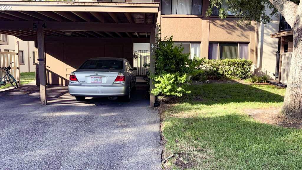 A silver sedan is parked under a covered carport next to a multi-story apartment building — 12922 WEDGEWOOD WAY UNIT A, HUDSON, FL