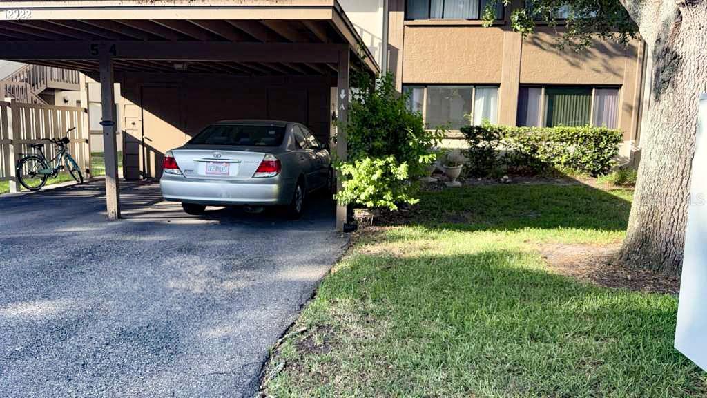 A silver sedan is parked under a covered carport next to a multi-story apartment building — 12922 WEDGEWOOD WAY UNIT A, HUDSON, FL